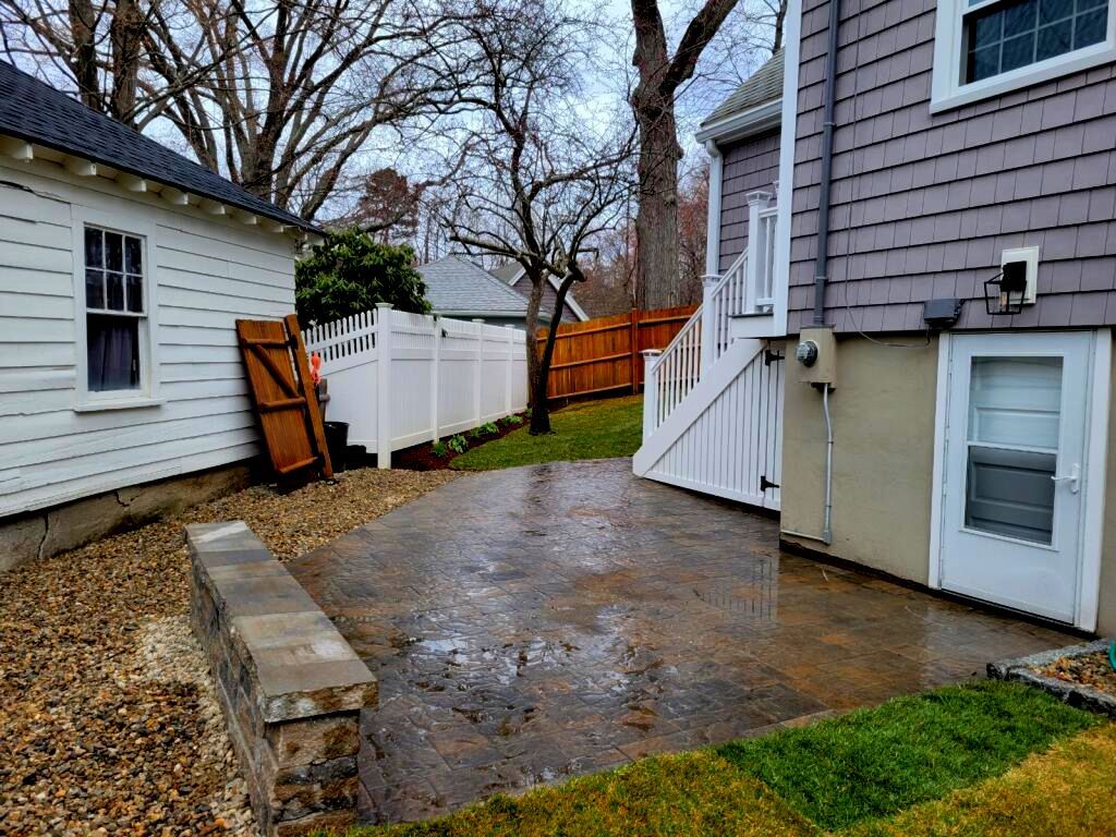 Backyard patio with gravel landscaping, white fence, and a shed.  A seating retaining wall was also installed
