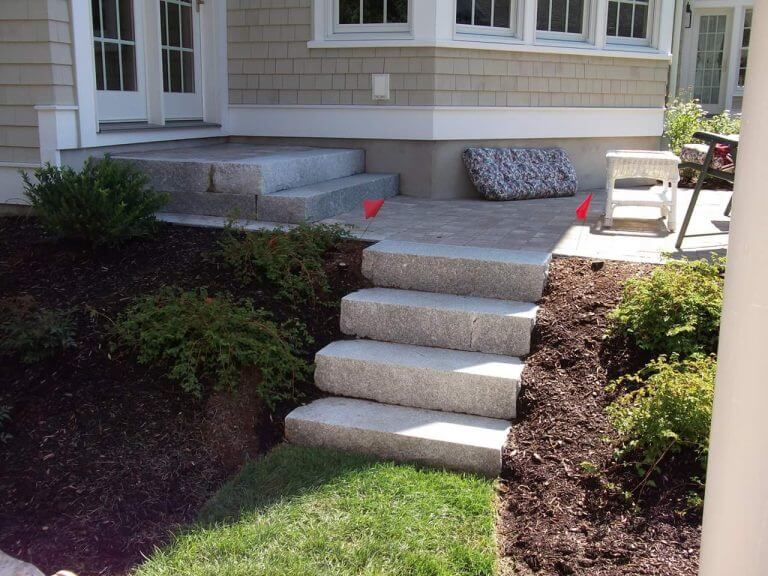 Granite steps leading up to a house with a raised patio, set in a landscaped yard.