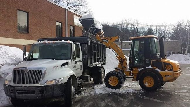 Photo of our snow plow lifting snow into a dump truck for commercial snow removal.