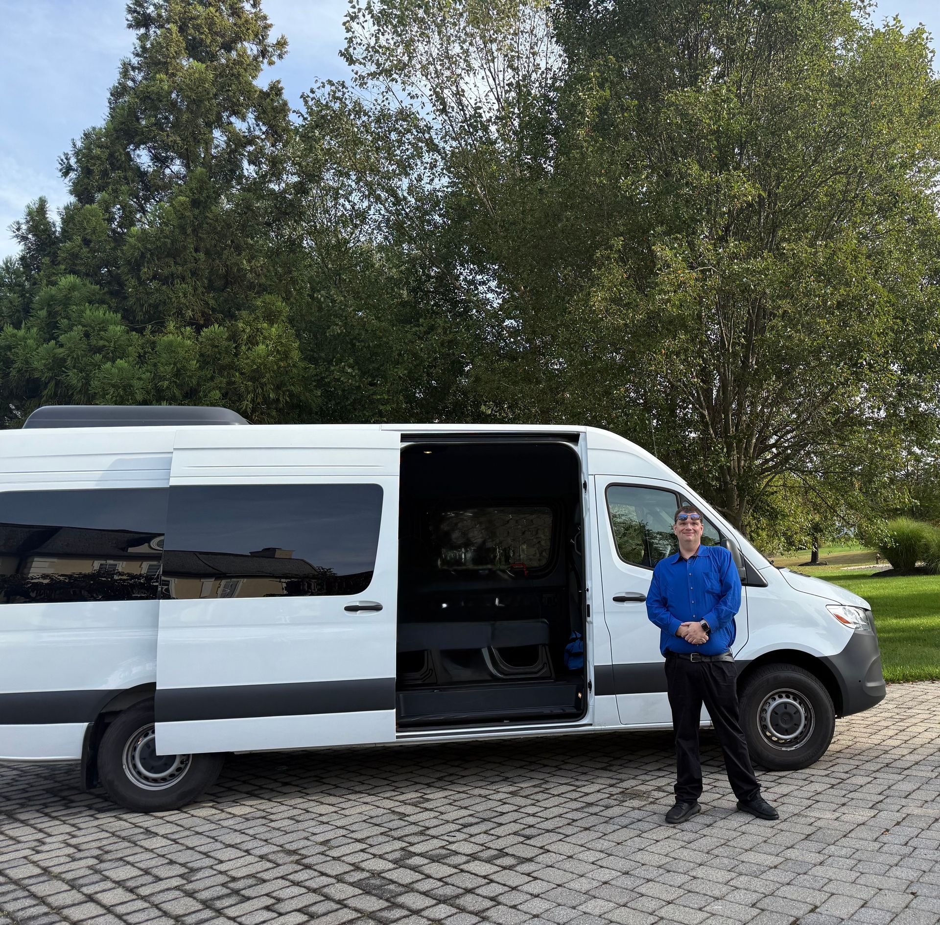 Man standing next to a white van with the side door open, trees in the background.