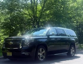 A black suv is parked on the side of the road in front of trees.