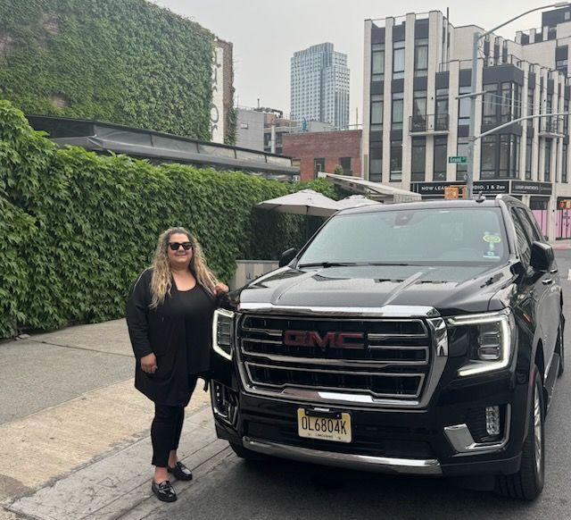 A woman is standing next to a black gmc truck