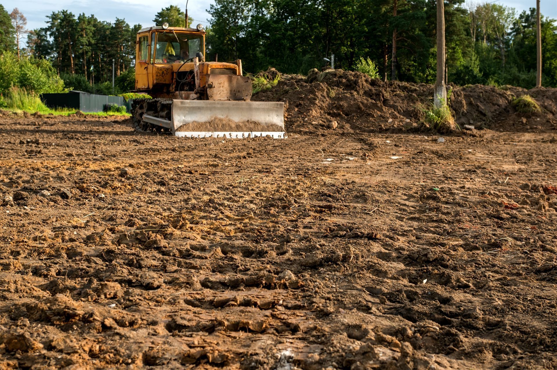 Bulldozer on a muddy construction site, clearing dirt. Trees and pile of dirt in the background.