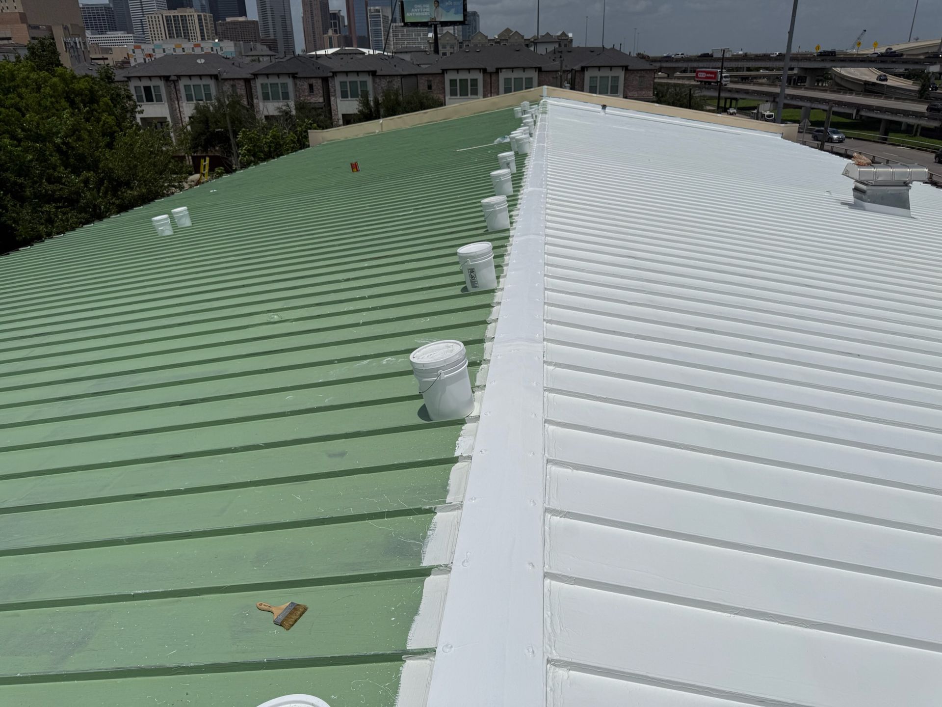Green and white metal roof with multiple vents, in an urban setting.