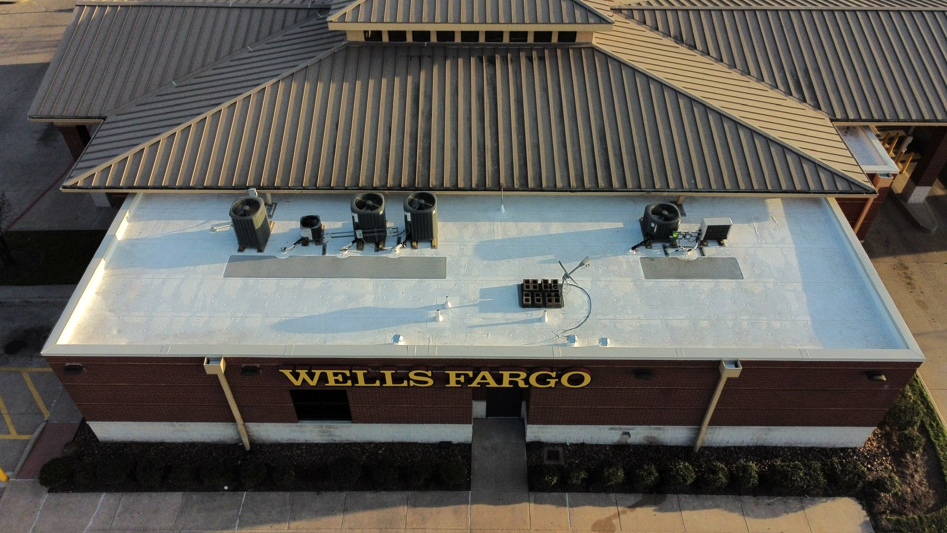 Exterior of a Wells Fargo bank building with a flat roof and air conditioning units. Brown and white facade.