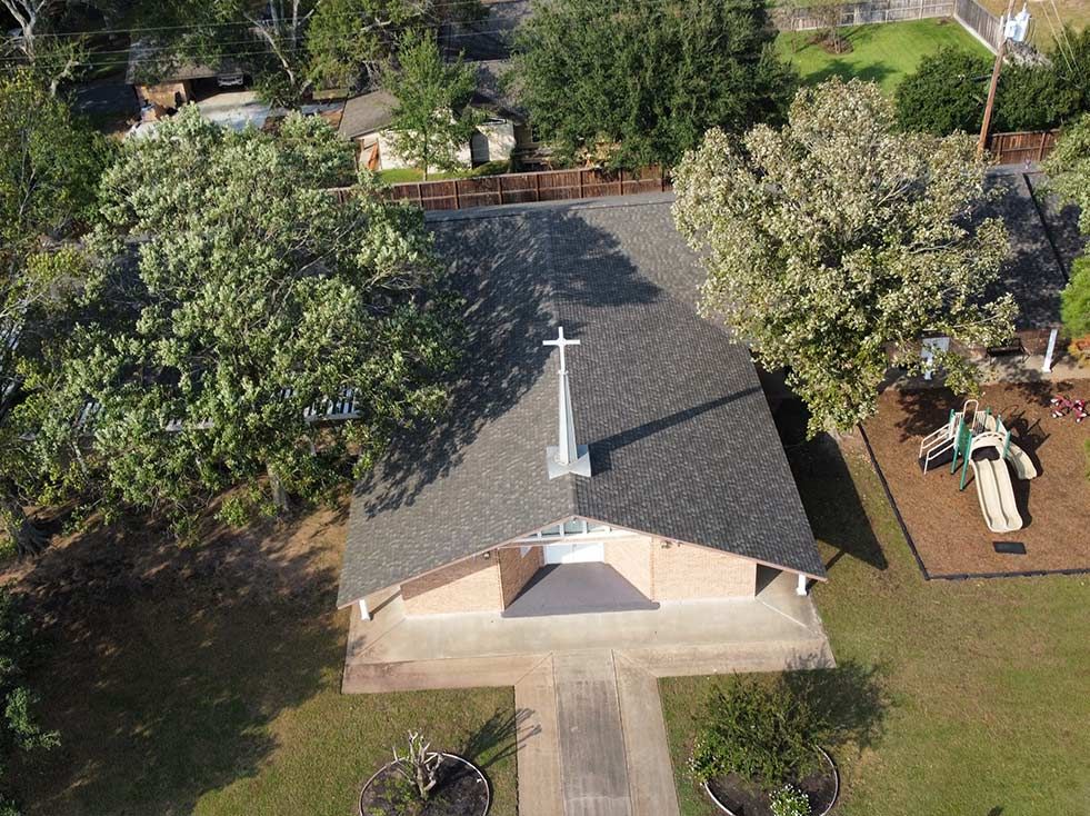 Aerial view of a church with a cross on the roof, surrounded by trees and a playground.