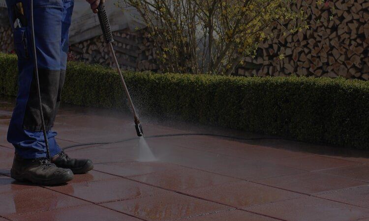 Person pressure washing a red brick patio.