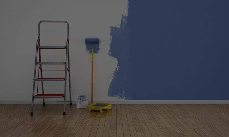 Ladder and paint supplies next to a wall partially painted blue.