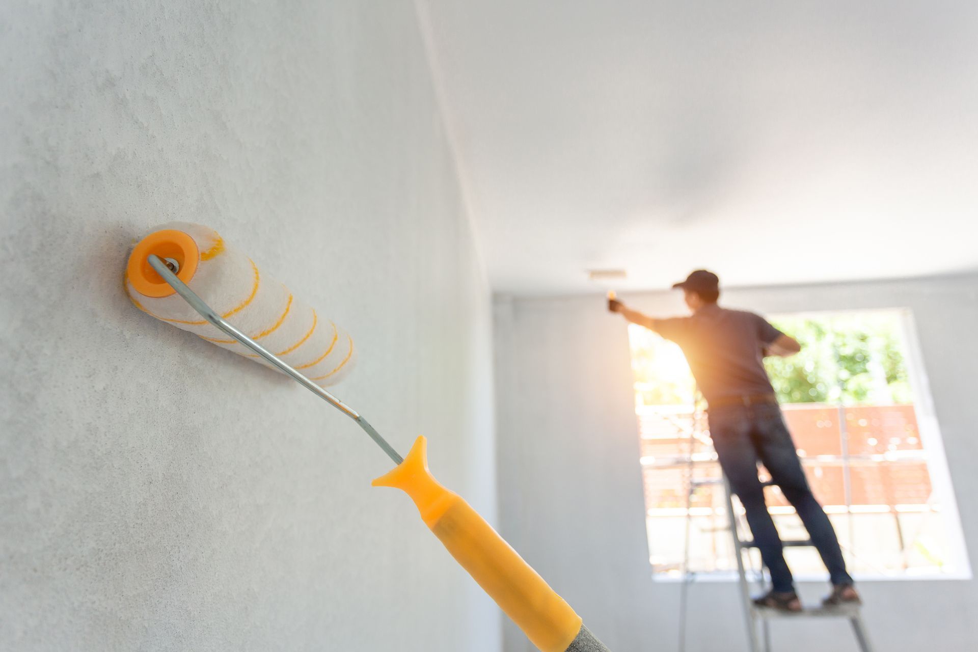 Close-up of a paint roller touching a wall as a painter works on the background. Close-up of a paint roller touching a wall as a painter works on the background.