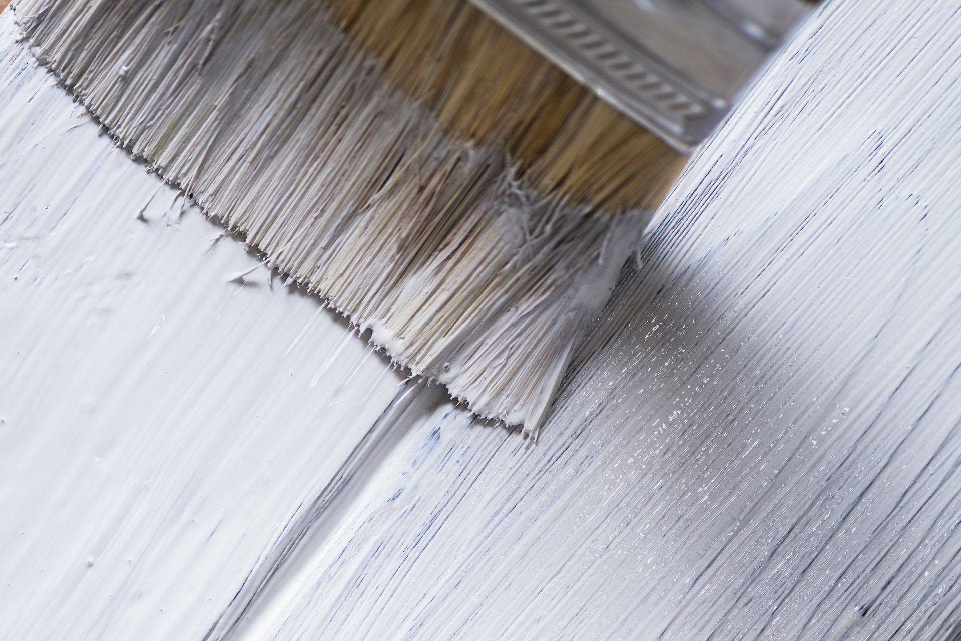 Closeup of a paintbrush painting with white paint on a wooden surface. Closeup of a paintbrush painting with white paint on a wooden surface.