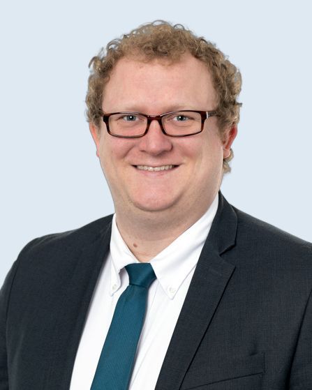 Man in glasses and suit smiles, head and shoulders portrait.