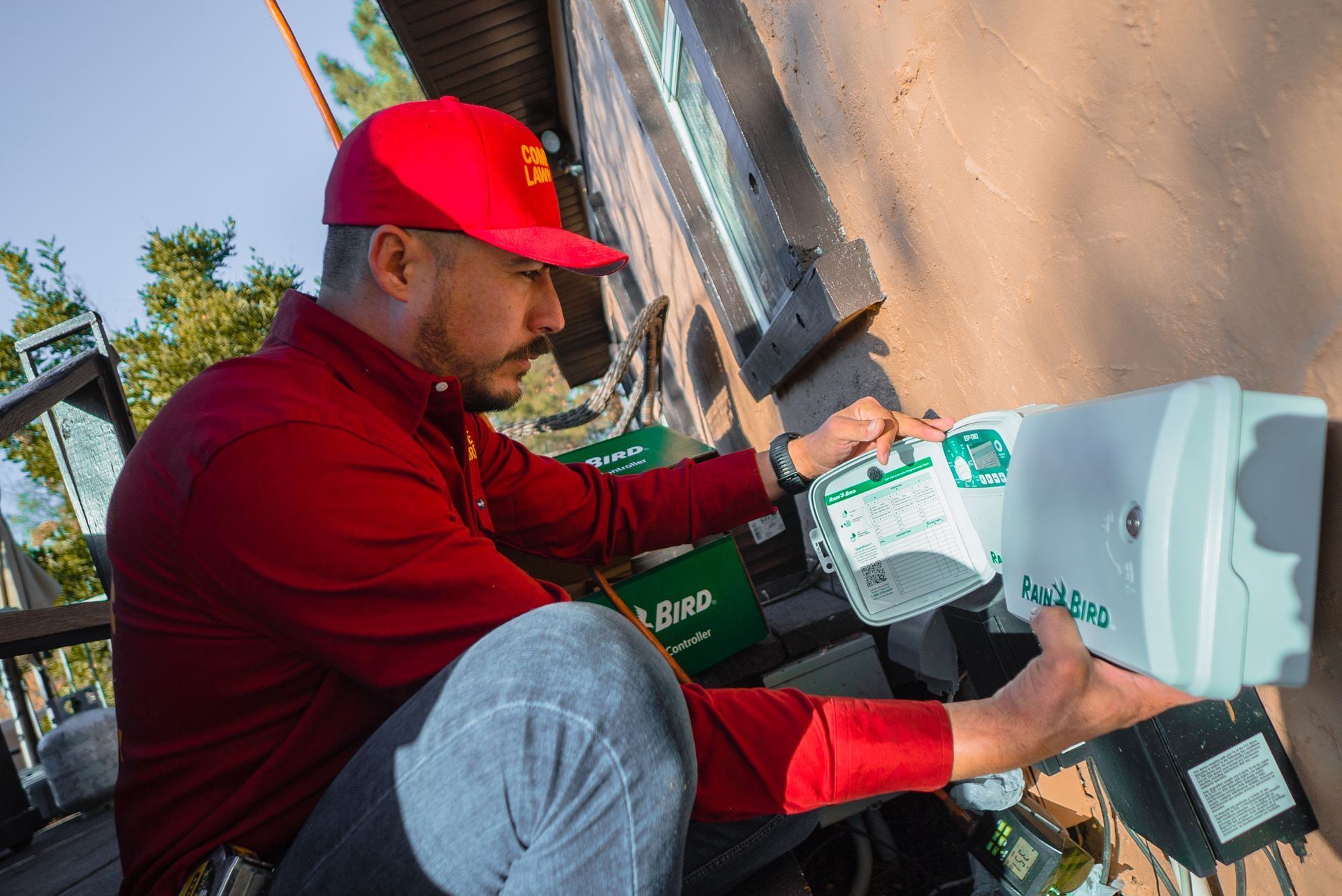 A man in a red shirt and red hat is working on a Rain bird lawn irrigation system.