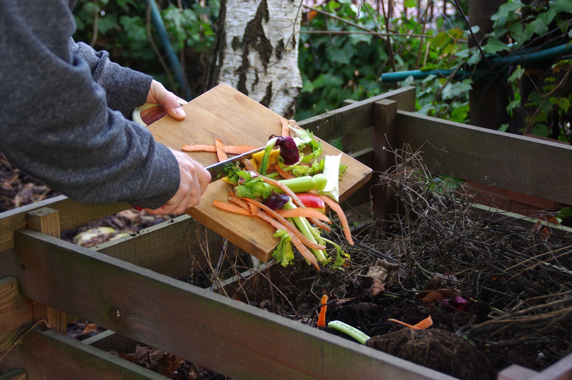 A person is cutting up vegetables on a cutting board in a compost bin.