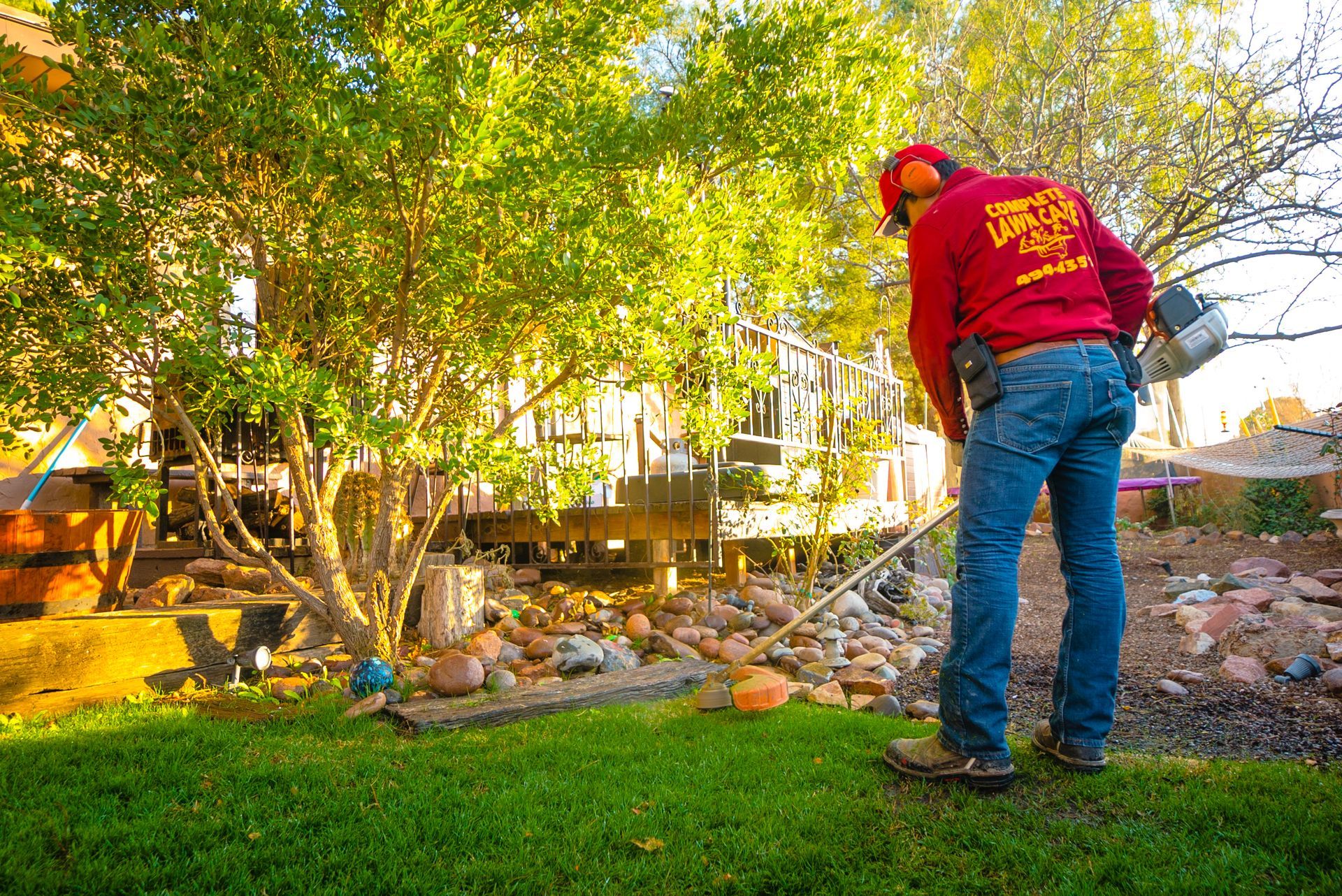 A man in a red shirt is standing in the grass cutting a tree.