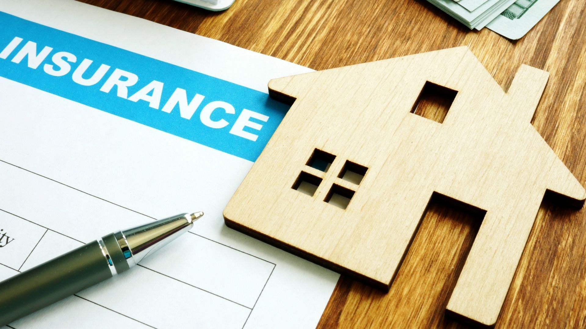 A wooden house is sitting on top of a piece of paper that says insurance.