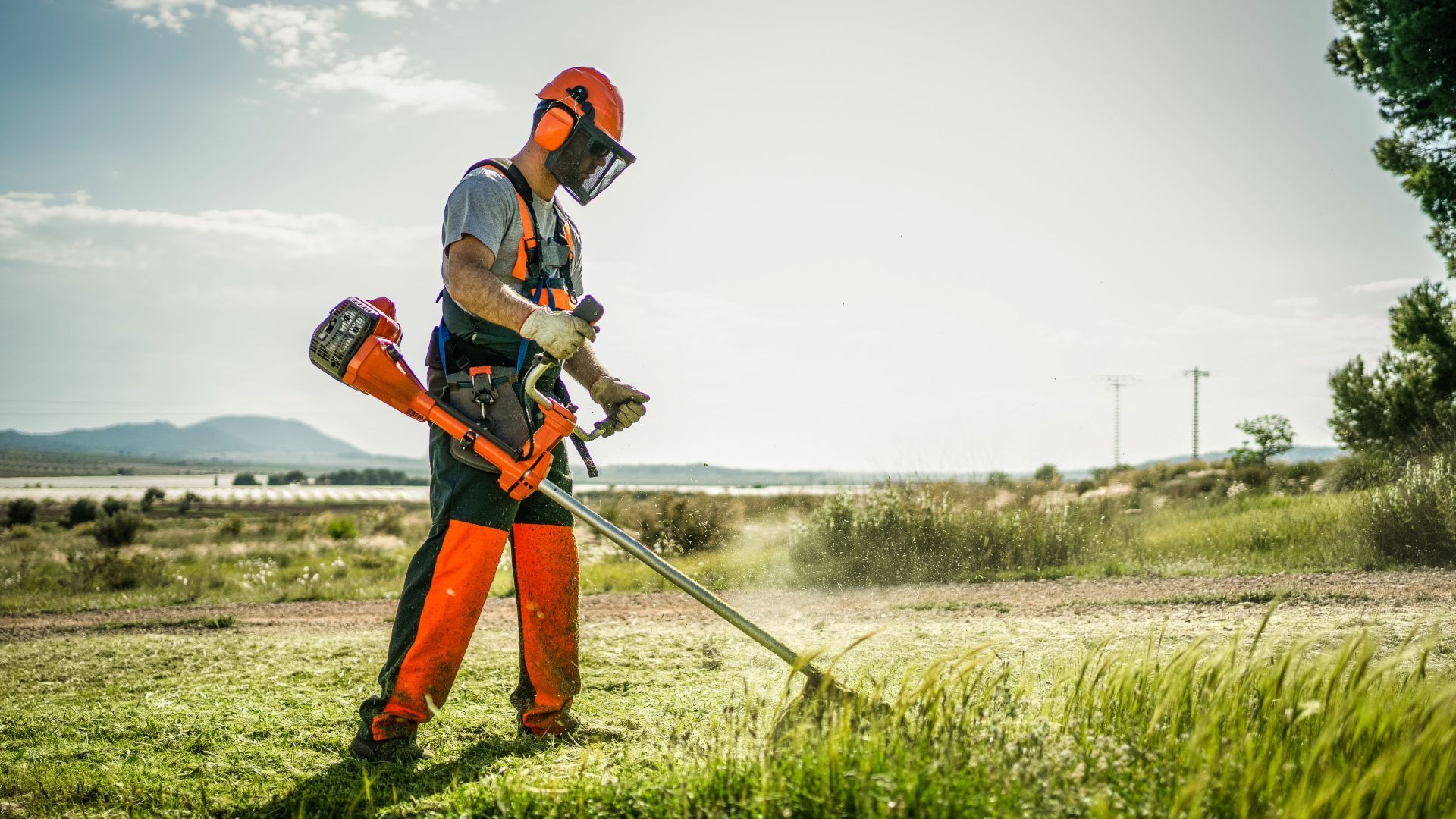 A man is cutting grass with a weed eater in a field.