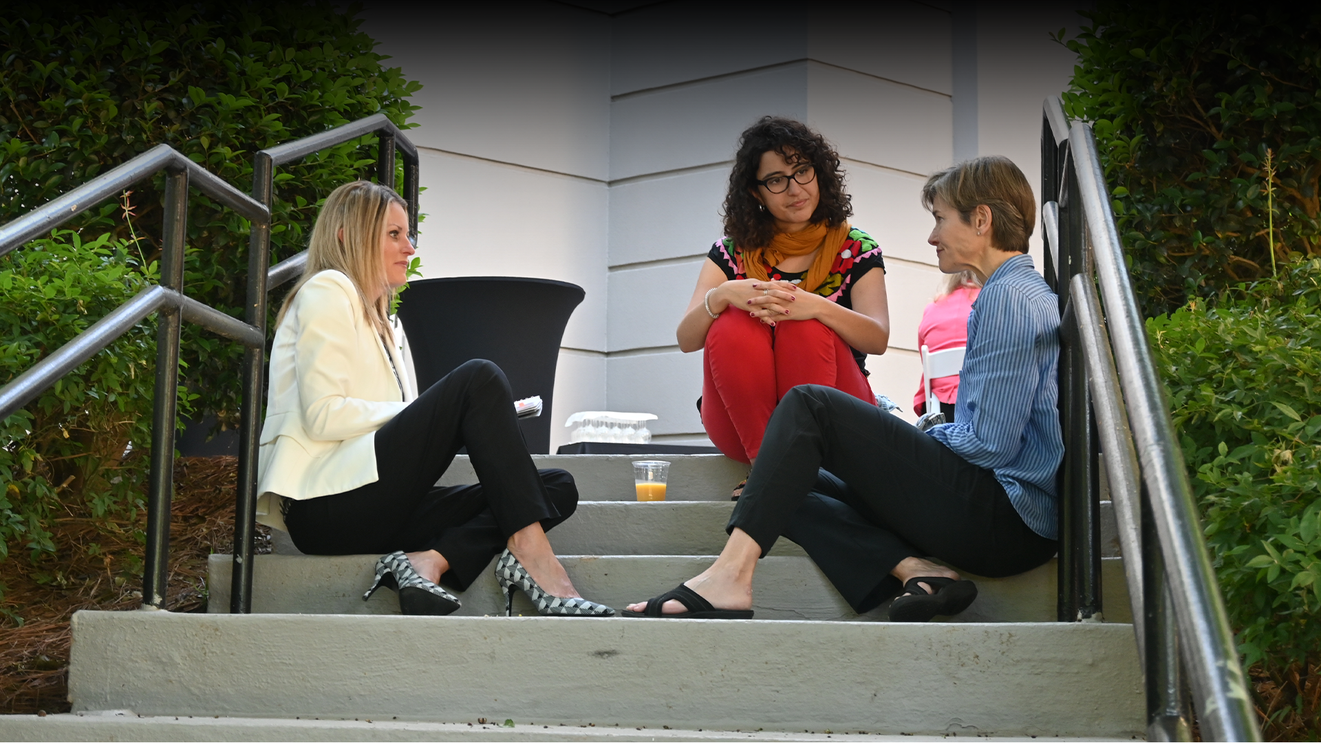 Three women are sitting on a set of stairs talking to each other