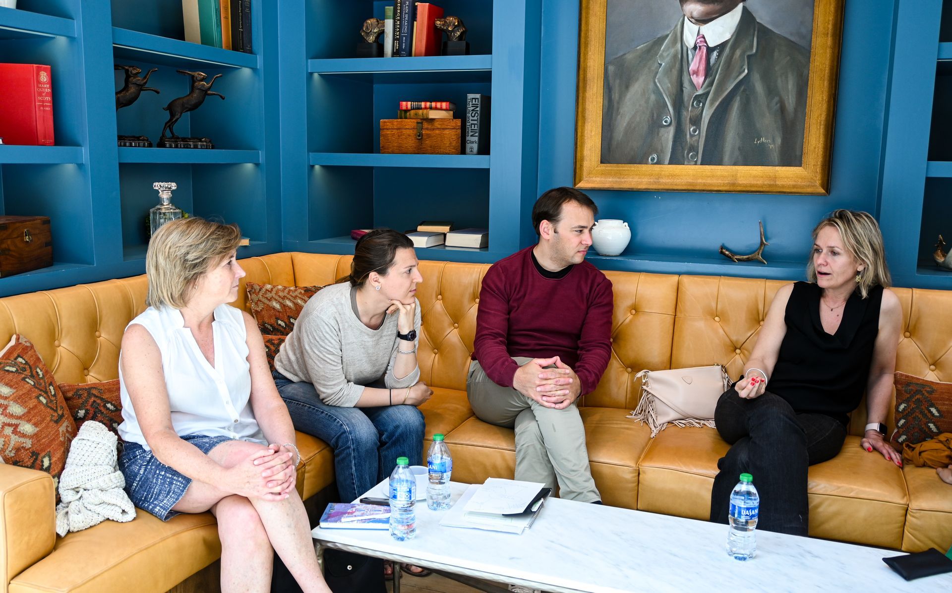 A group of people are sitting on a couch in front of a painting.