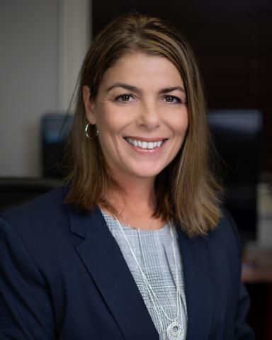 A woman in a suit and necklace is smiling for the camera.