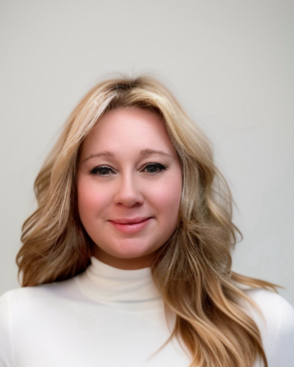 A woman with long blonde hair is wearing a white turtleneck and smiling.