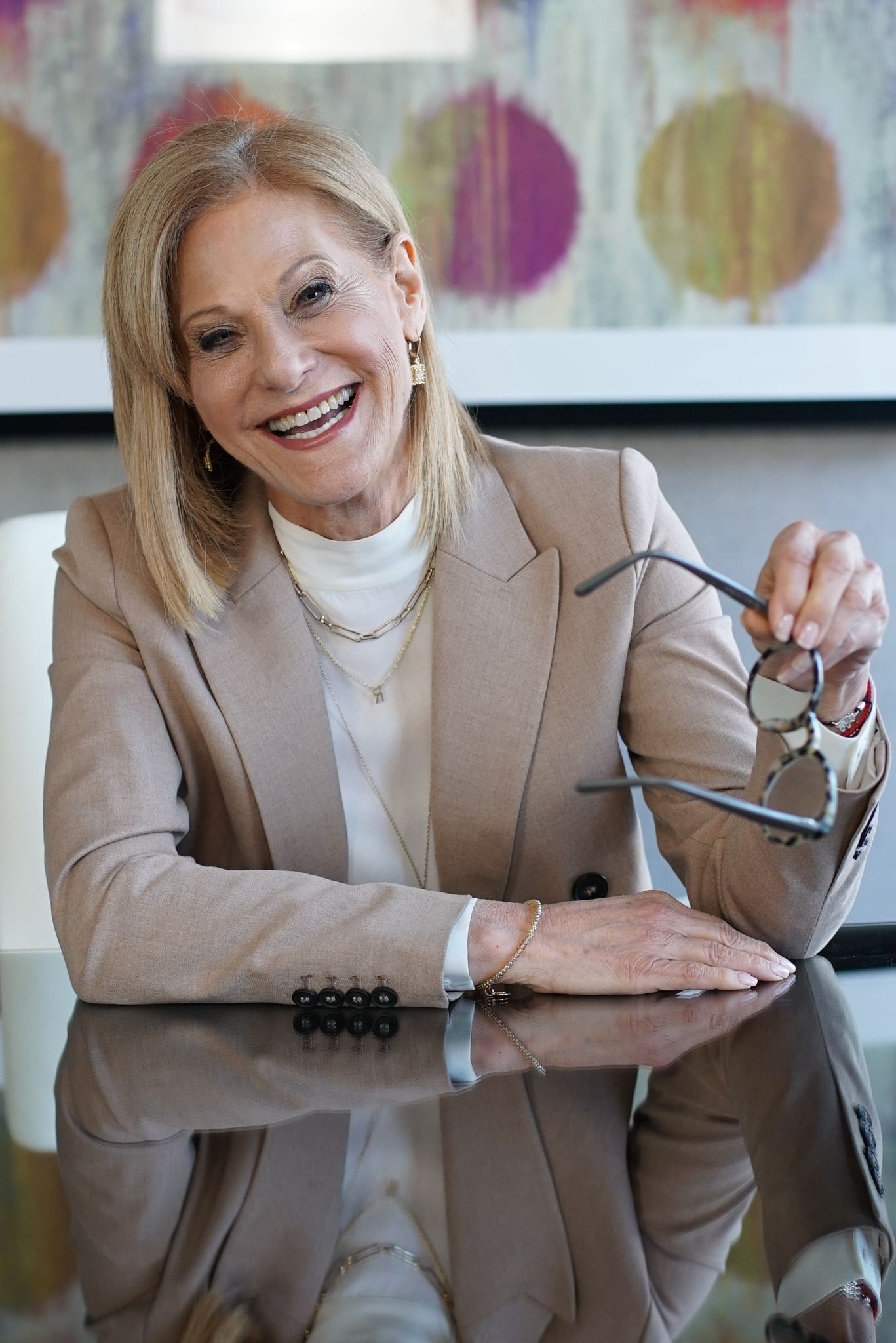 A woman is sitting at a table with her arms crossed and smiling.