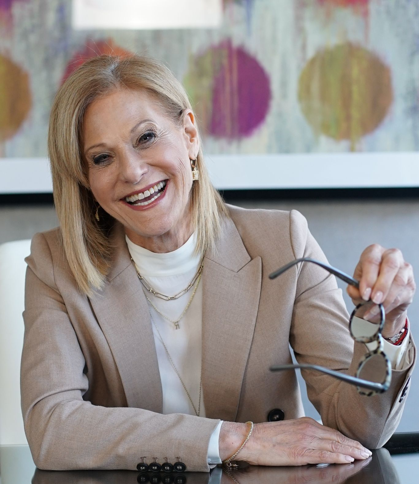 A woman is sitting at a table with her arms crossed and smiling.