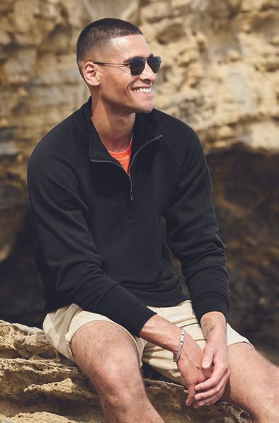 Ένας άντρας που φοράει γυαλιά ηλίου και μαύρη μπλούζα κάθεται σε έναν βράχο.