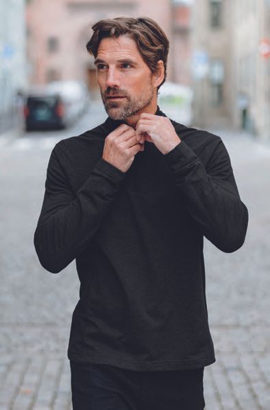 Ένας άντρας με μαύρο πουκάμισο στέκεται σε έναν πλακόστρωτο δρόμο.