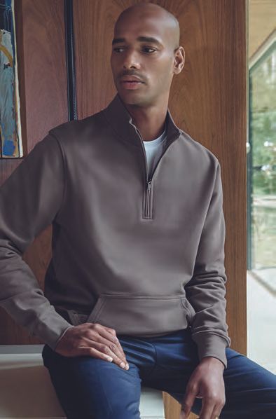 Ένας άντρας με καφέ πουλόβερ κάθεται σε ένα σκαμπό μπροστά σε ένα παράθυρο.