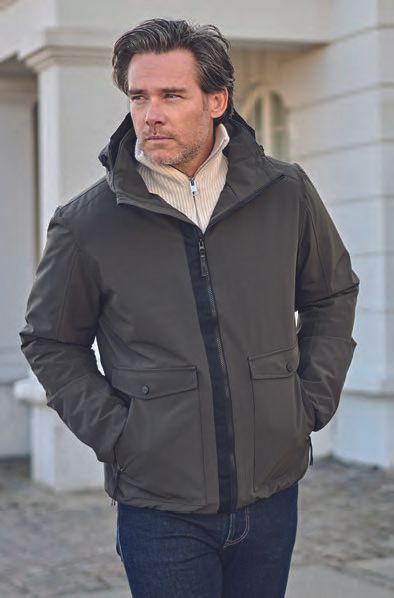 Ένας άντρας που φοράει πράσινο μπουφάν και τζιν στέκεται μπροστά σε ένα κτίριο.