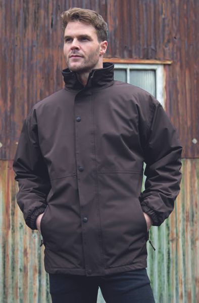 Ένας άντρας που φοράει καφέ σακάκι στέκεται μπροστά σε ένα ξύλινο κτίριο.