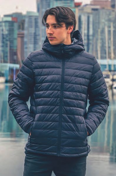 Ένας νεαρός άνδρας που φοράει μπλε μπουφάν με κουκούλα στέκεται μπροστά σε μια πόλη.