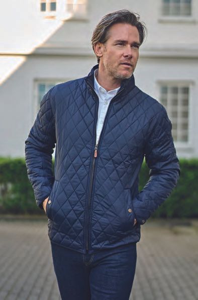 Ένας άντρας που φοράει ένα μπλε καπιτονέ μπουφάν στέκεται μπροστά σε ένα κτίριο.