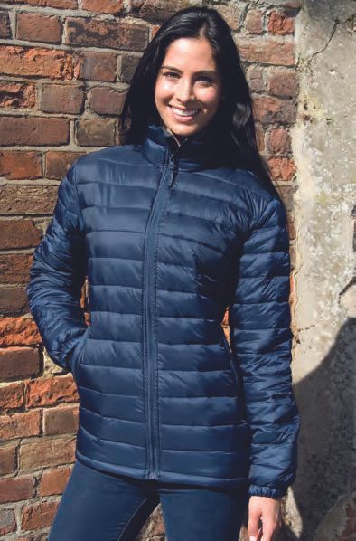 Μια γυναίκα που φοράει μπλε μπουφάν στέκεται μπροστά σε έναν τοίχο από τούβλα.