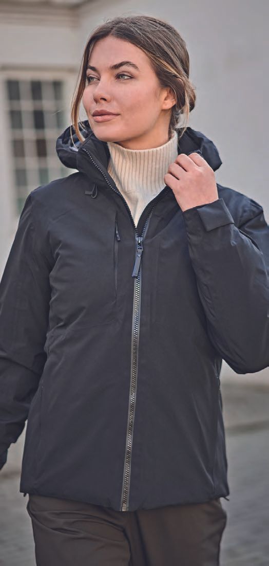 Μια γυναίκα που φοράει μαύρο σακάκι και λευκό ζιβάγκο στέκεται μπροστά σε ένα κτίριο.