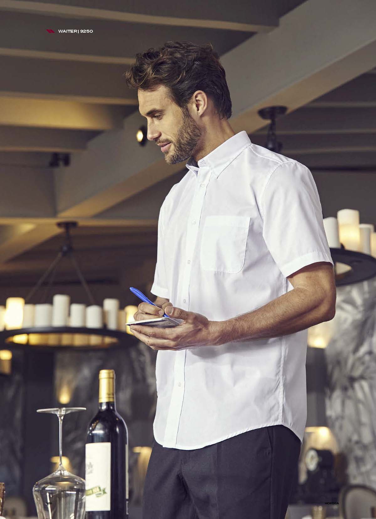 Ένας άντρας με λευκό πουκάμισο στέκεται σε ένα εστιατόριο κρατώντας ένα κινητό τηλέφωνο.