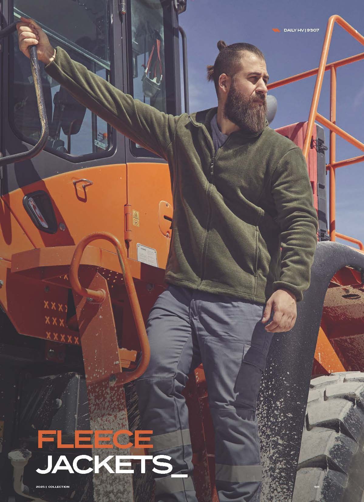 Ένας άντρας με γένια στέκεται μπροστά από ένα τρακτέρ φορώντας ένα φλις μπουφάν