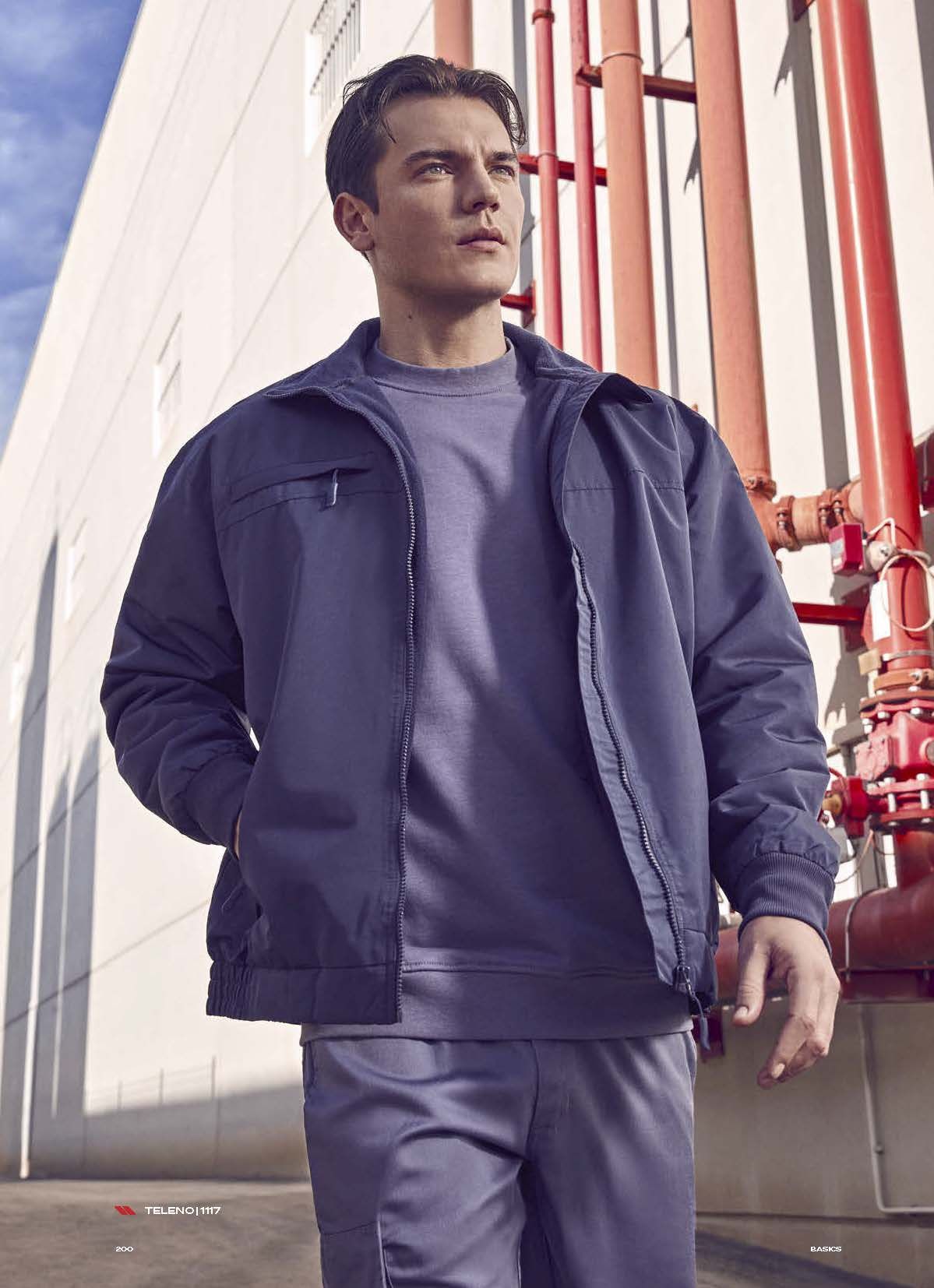 Ένας άντρας που φοράει μωβ σακάκι και μωβ φούτερ στέκεται μπροστά σε κόκκινους σωλήνες.