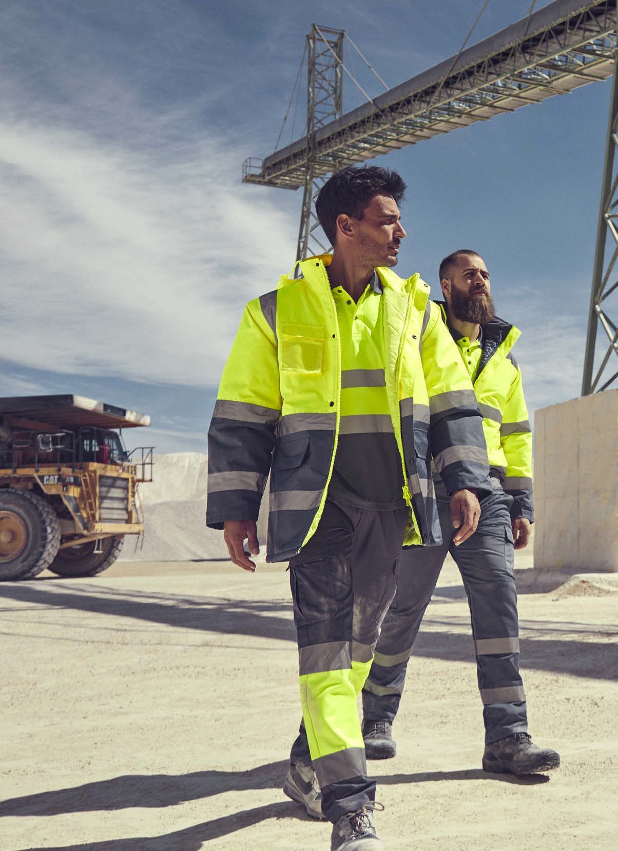 Man working in an industrial setting wearing grey work trousers and a blue short-sleeve Roly work t-shirt, featuring functional pockets and ergonomic fit.