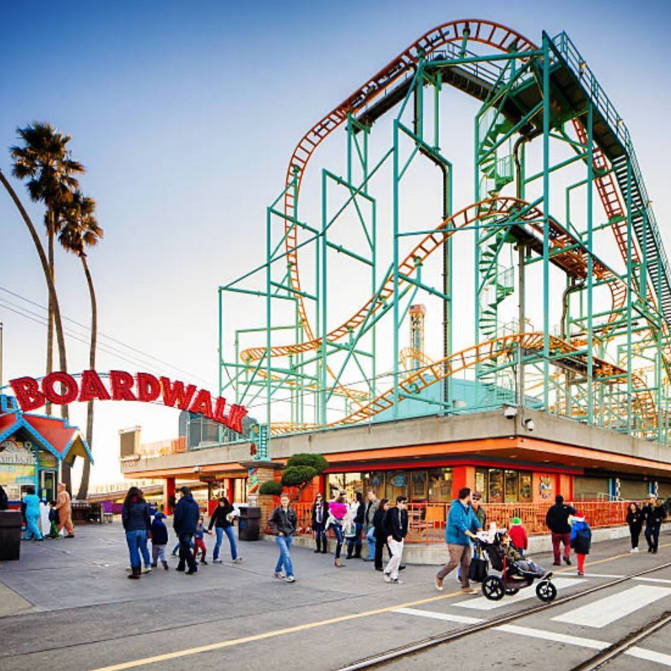 People are walking in front of a roller coaster at the boardwalk
