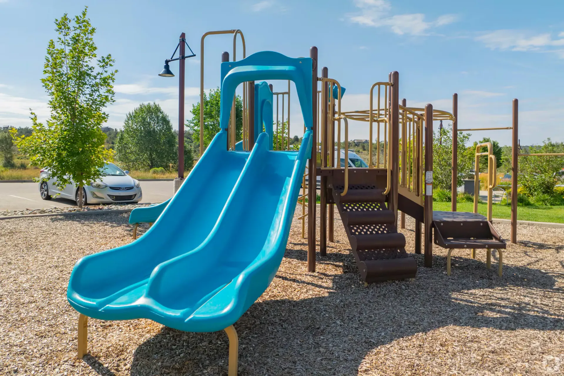 Outdoor playground with a bright blue double slide and climbing structure on a wood-chip surface.