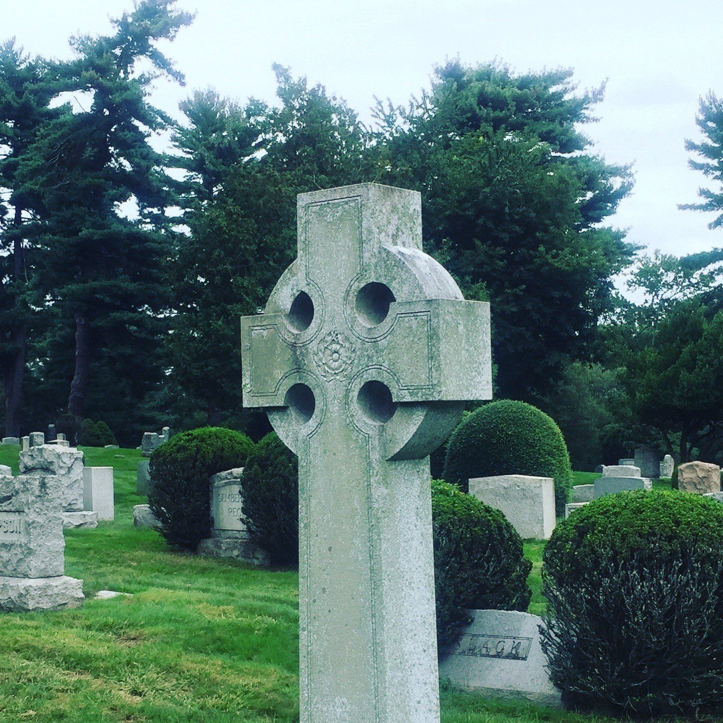 A stone cross in a cemetery with trees in the background