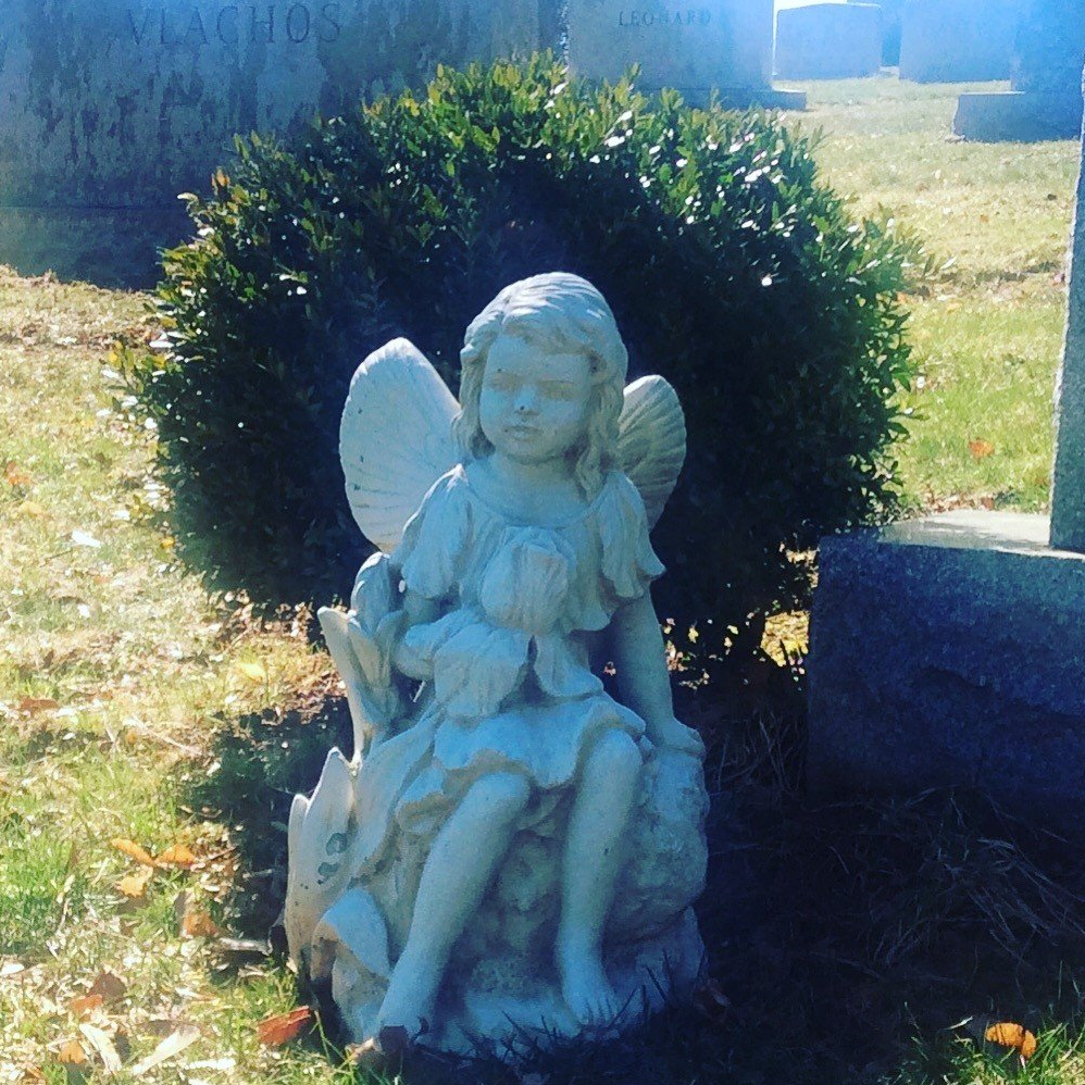 A statue of a fairy sitting on a rock in a cemetery