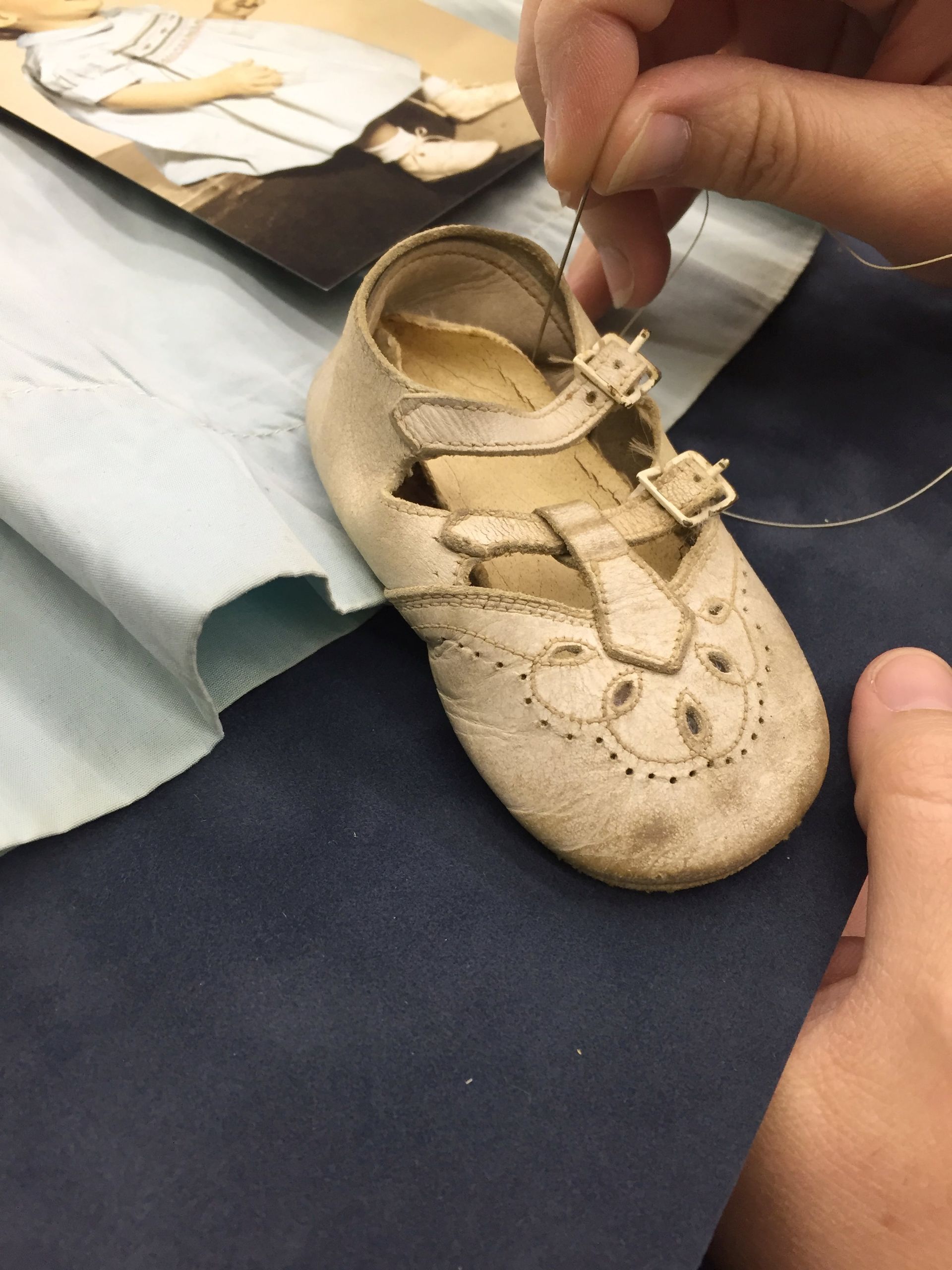 Close-up of a small, worn, cream-colored shoe being sewn by a person's hand.