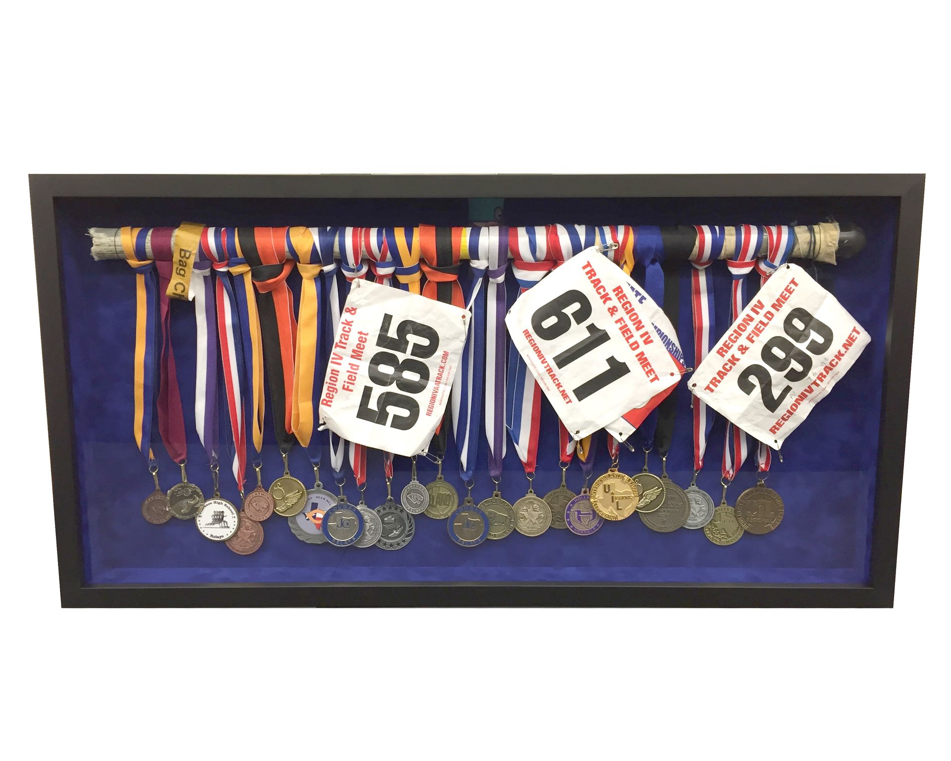 Black shadow box displays running medals, ribbons, and bibs (numbers 585, 611, and 299) against a blue backdrop.