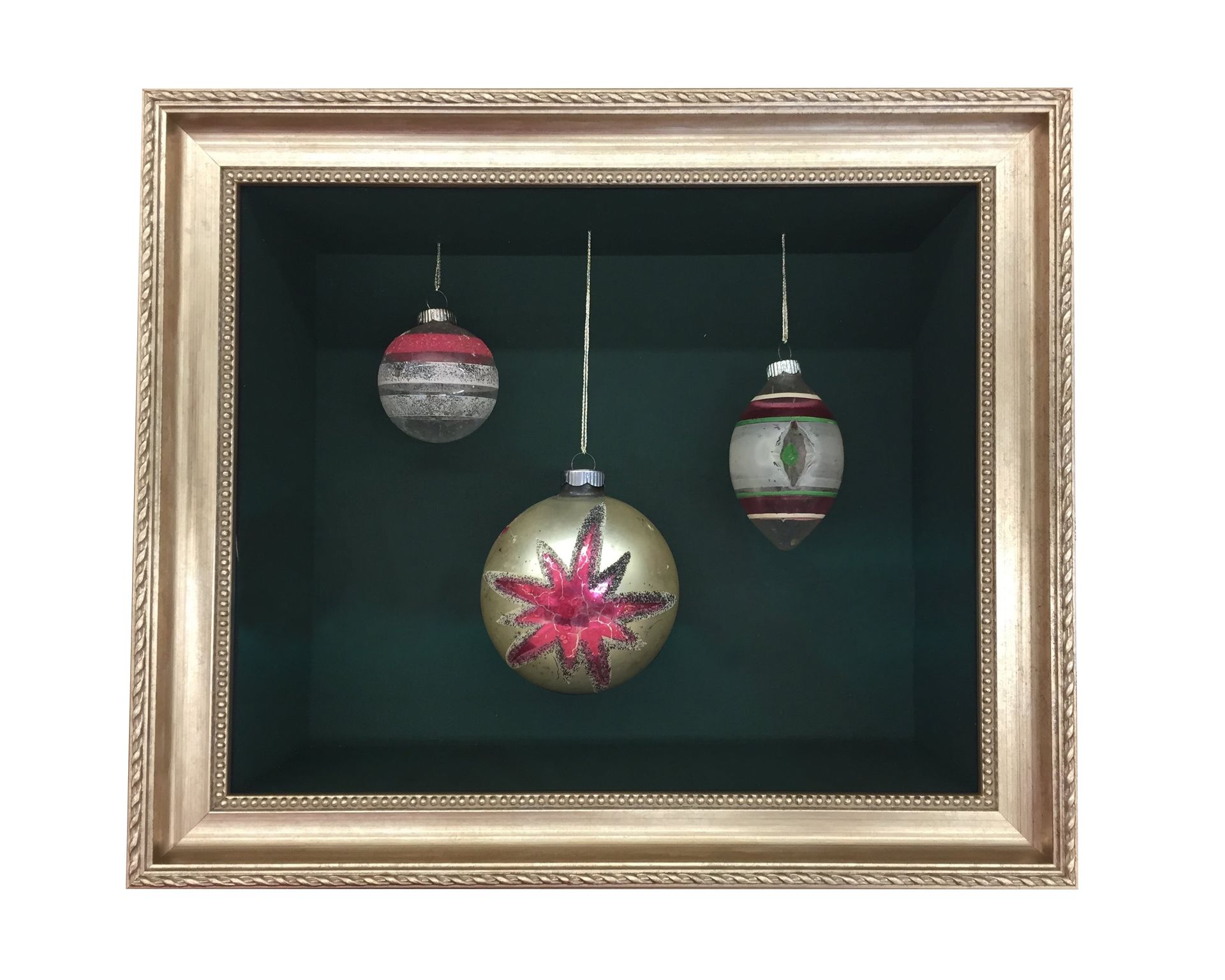 Three vintage Christmas ornaments hanging in a shadowbox with gold frame.