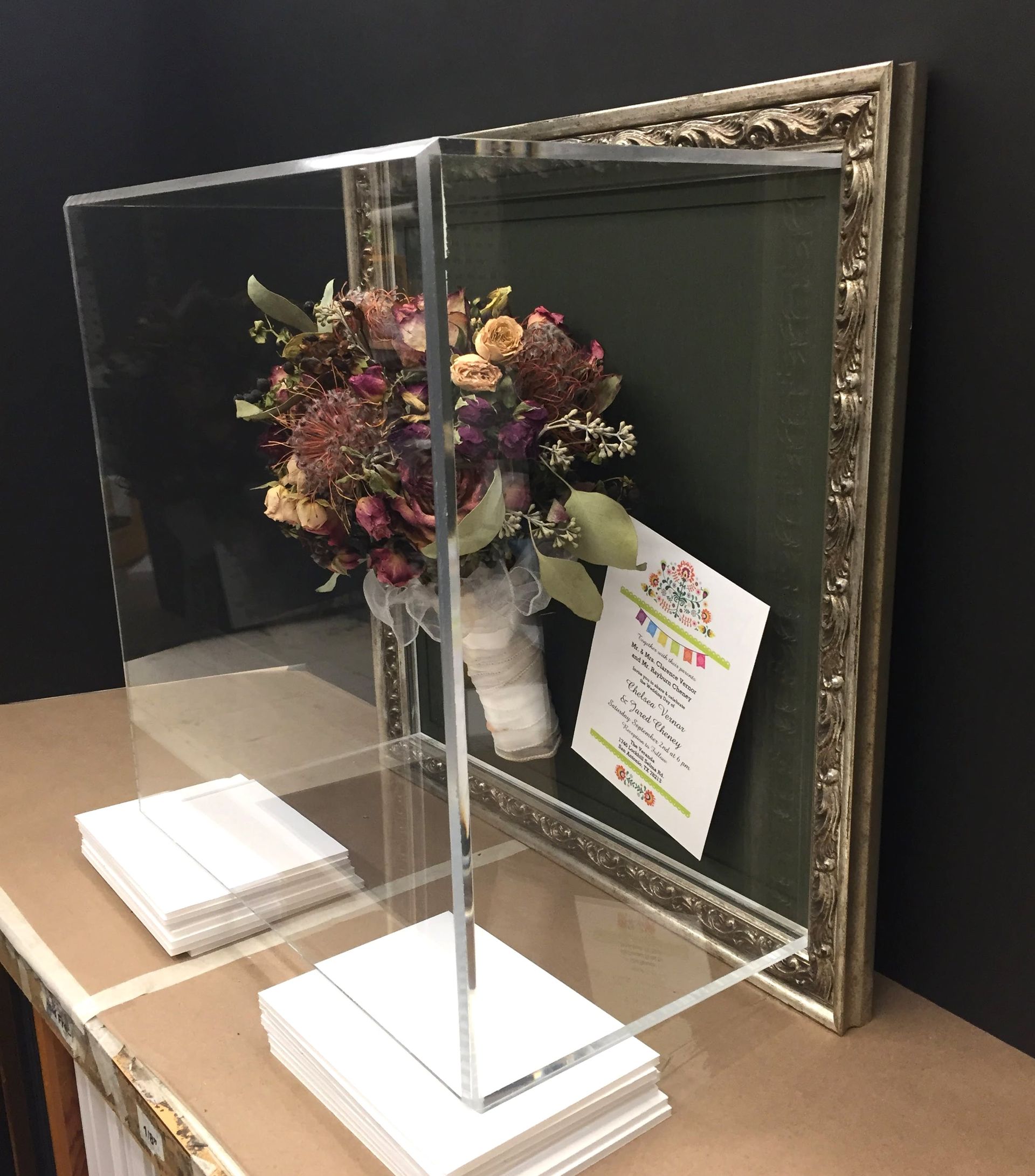 Clear acrylic display case holding a bouquet of flowers with a framed card.