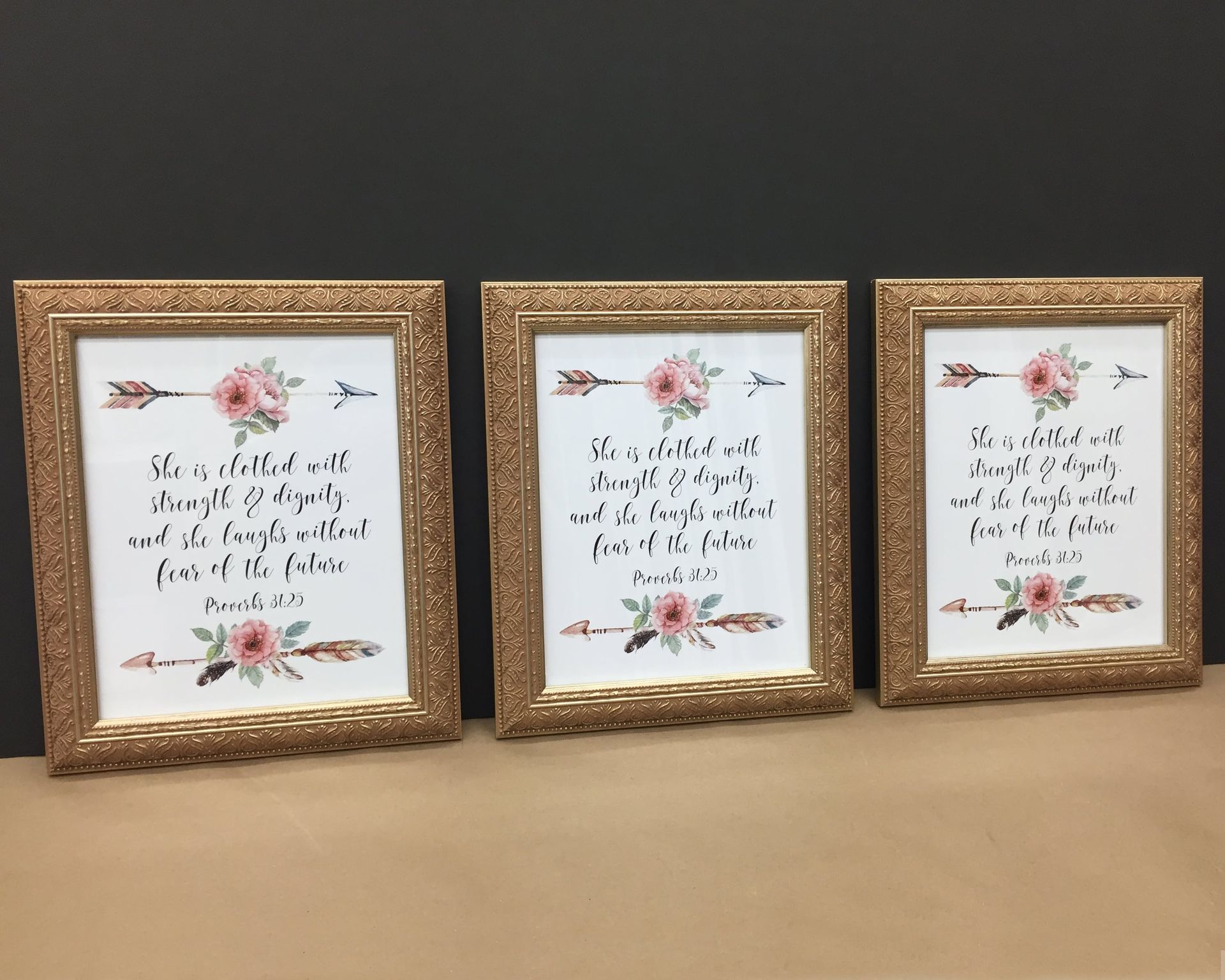Three framed art prints with floral and arrow designs, gold frames, and scripture quotes on a neutral background.