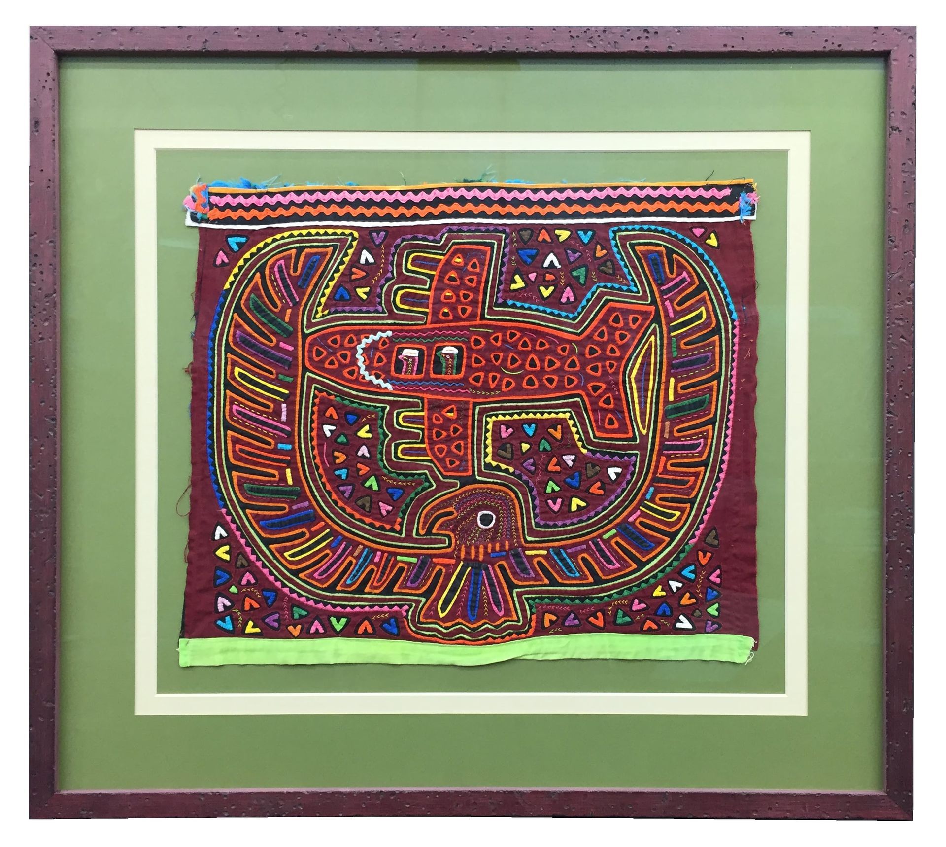 Framed textile art with red bird-like figure and intricate stitching. Framed in green with a brown border.
