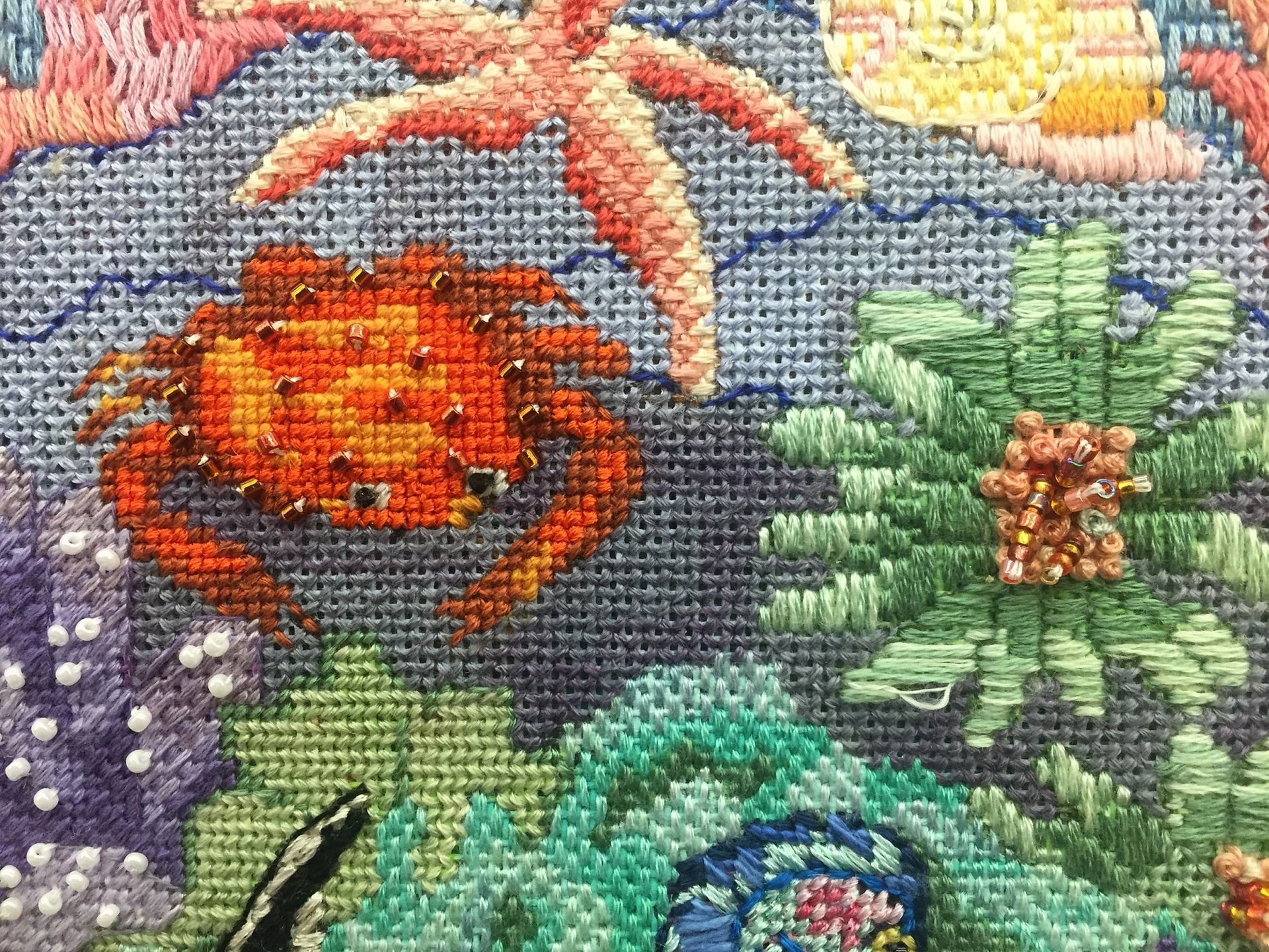 Needlepoint of an orange crab, starfish, and coral on a blue background.